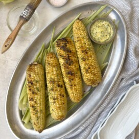 A pewter platter of golden grilled corn with herb butter.