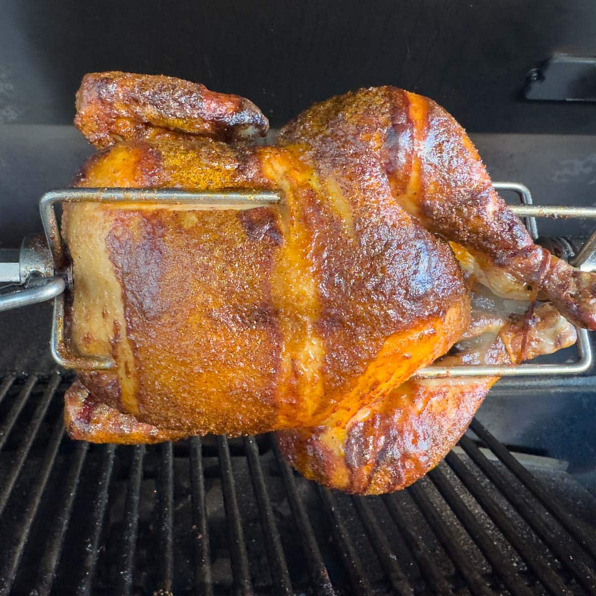 Golden brown chicken on a rotisserie grill with silver meat forks.