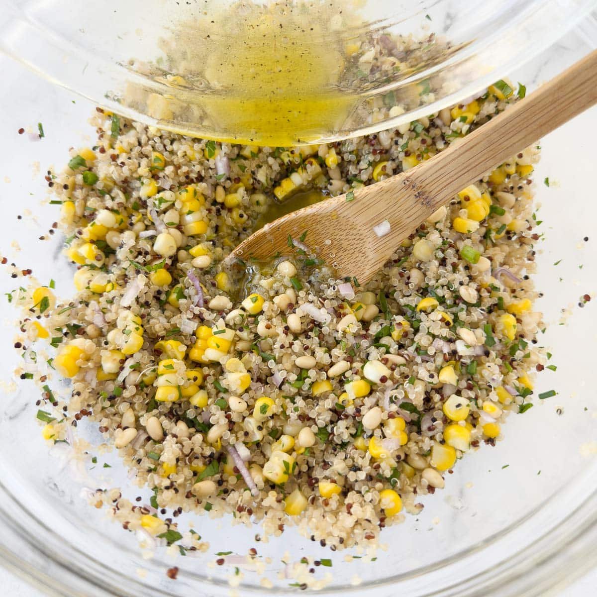 Grain bowl salad being mixed with corn, herbs, pine nuts, and vinaigrette.