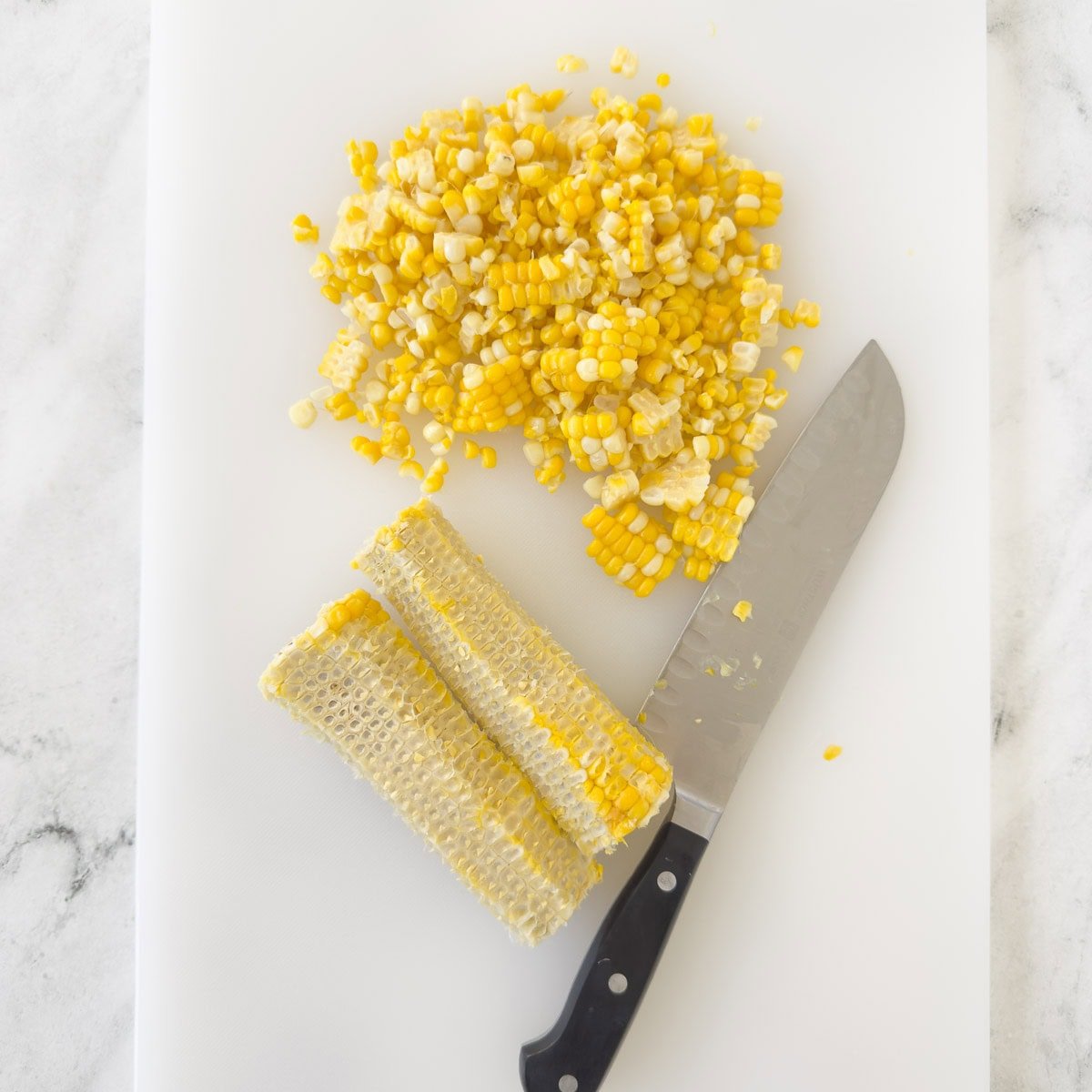 Cooked corn on the cob, sliced off on a cutting board with a knife.