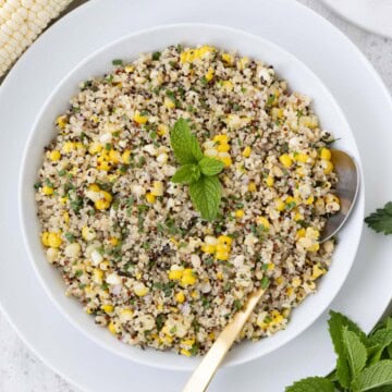 Quinoa and corn salad in white bowl with mint and a gold spoon.
