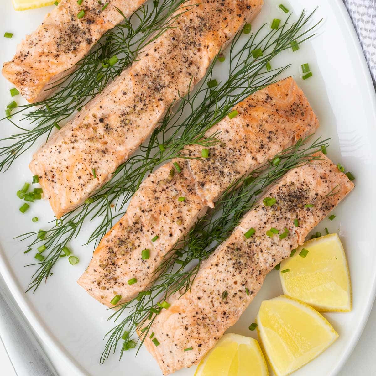 Close up of a platter of salmon filets with lemon and herbs on a table.