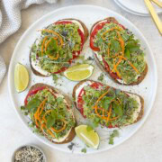 Avocado tomato toast with baby greens on top and basil leaves.