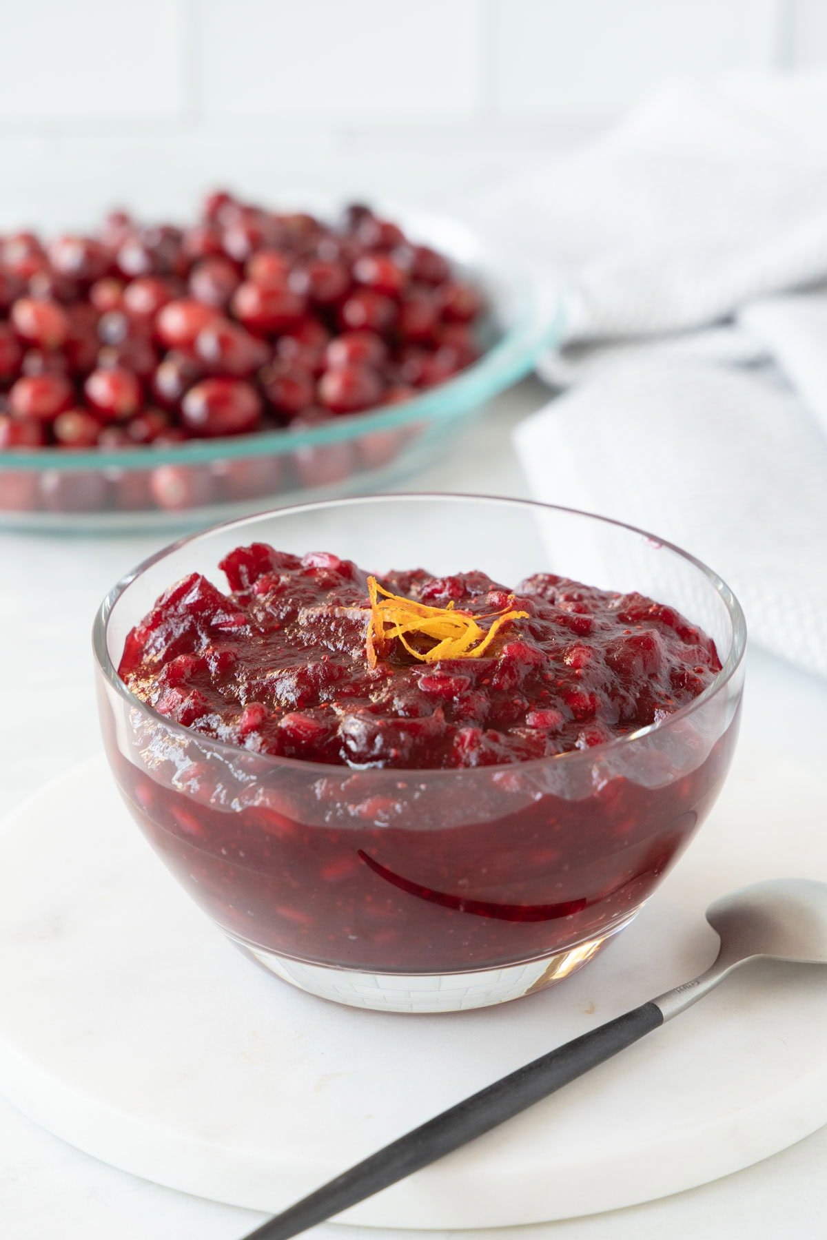 A glass bowl of deep red cranberry sauce topped with orange zest garnish.