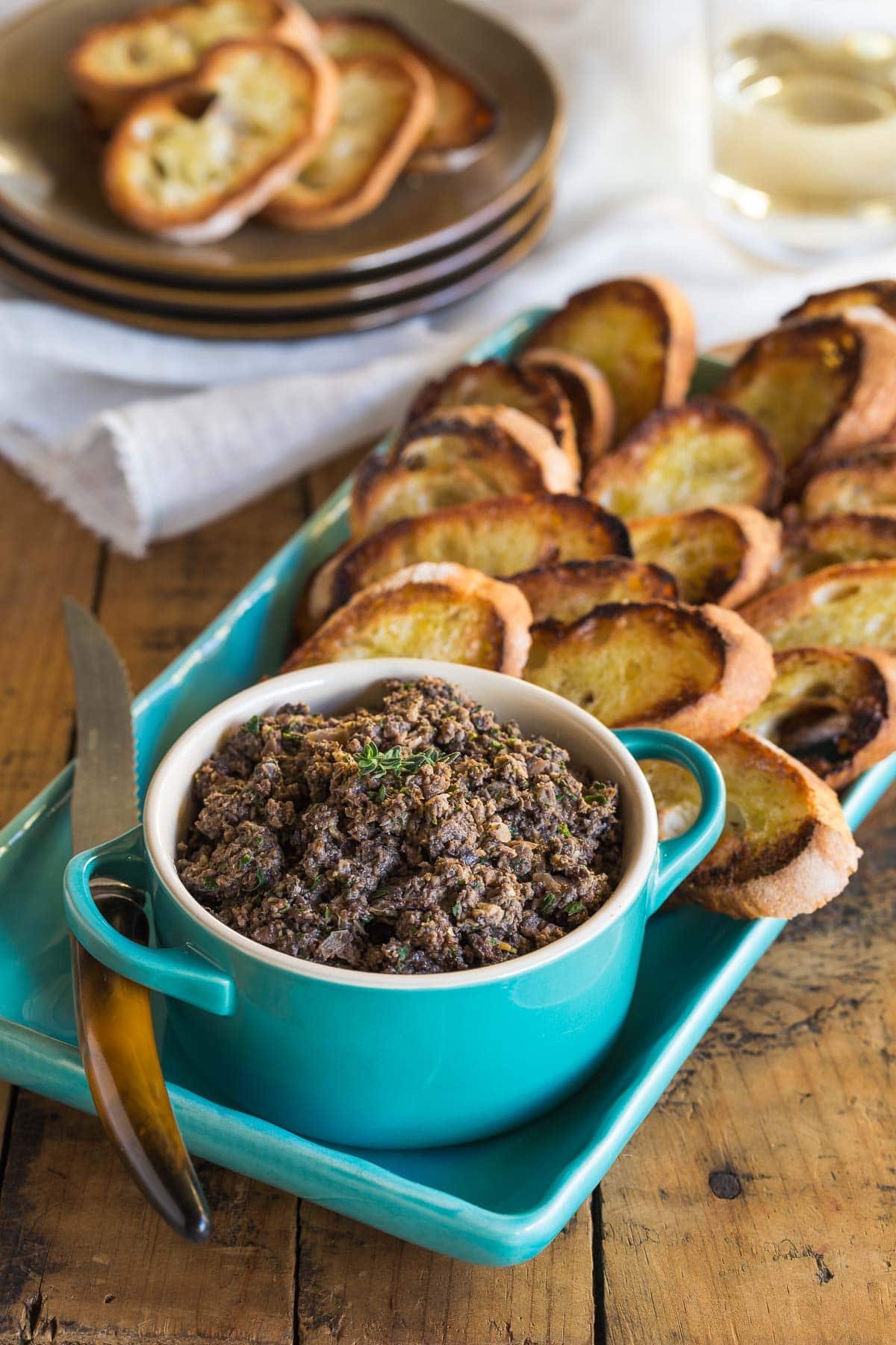 A small blue bowl of mushroom duxelles with crisp crostini on a platter.