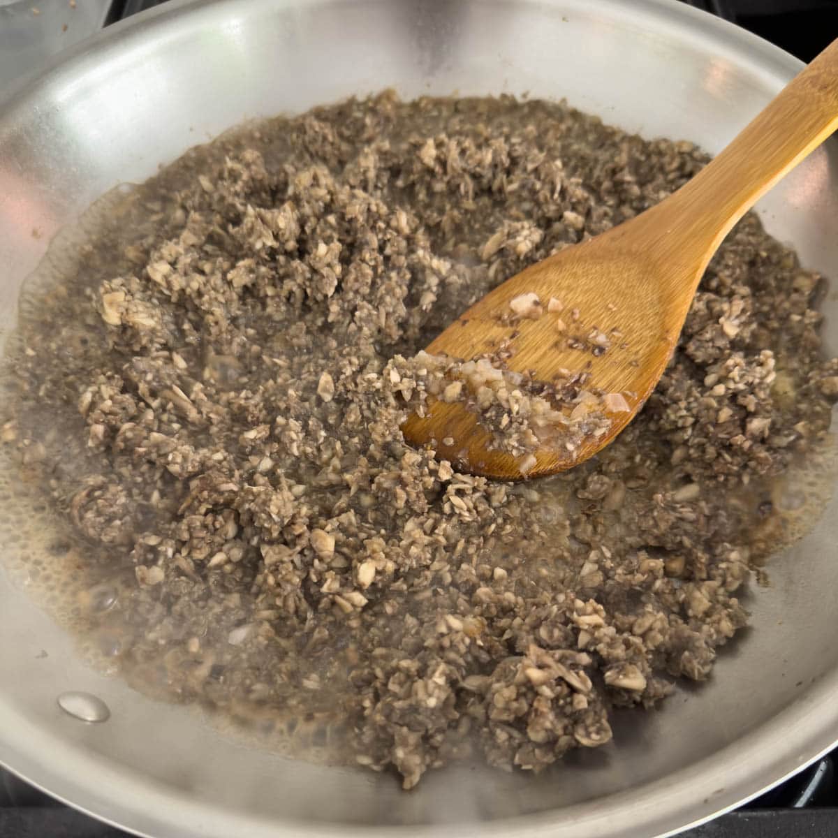Chopping mushroom cooking for duxelles in a fry pan.