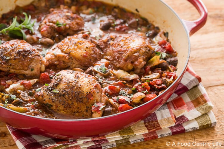 Braised chicken thighs in a pan with vegetables.