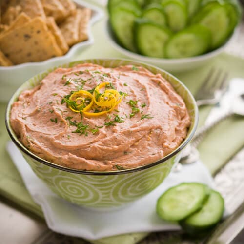 Creamy smoked salmon dip with crackers and cucumbers on a serving tray.