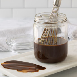 A jar of rich brown hoisin sauce in a jar with a silver whisk.