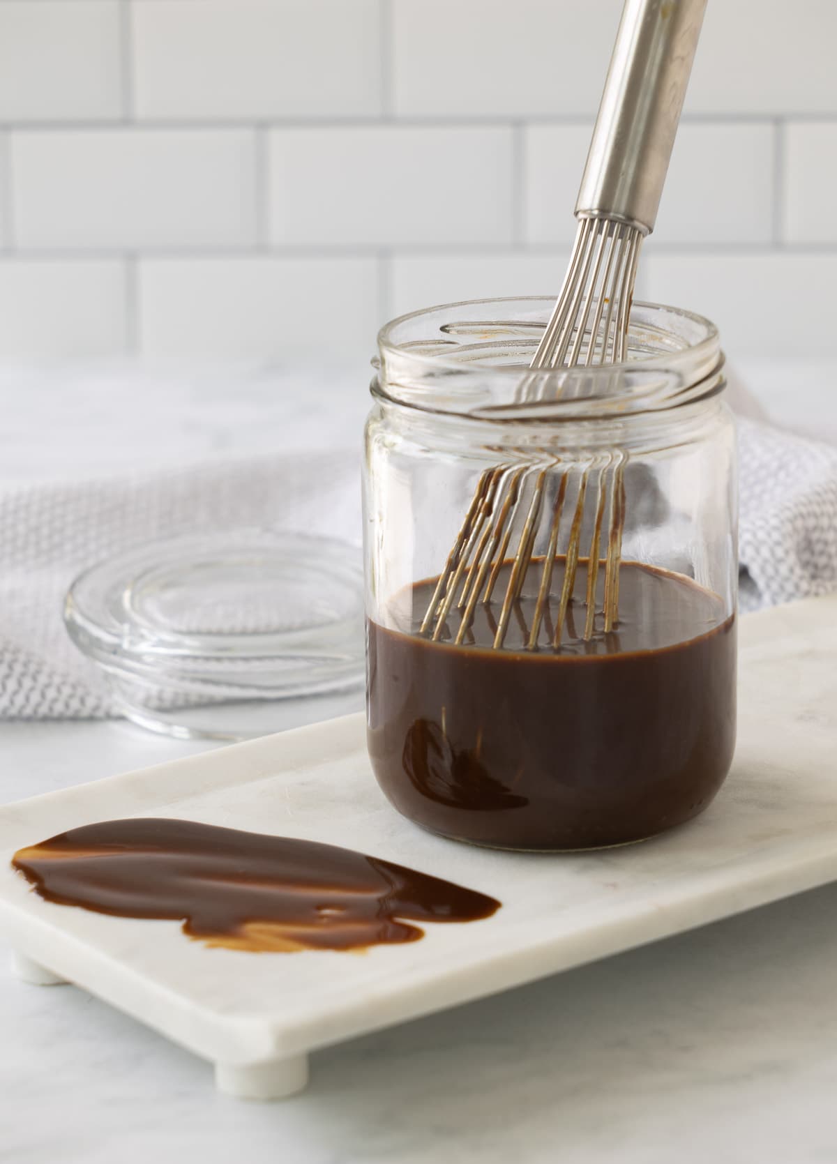 A jar of rich brown hoisin sauce in a jar with a silver whisk. 