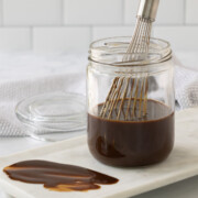 A glass jar with rich brown hoisin sauce and a whisk for mixing.