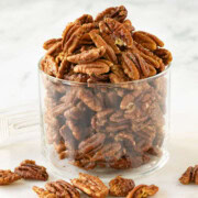 A jar of golden glazed pecans on a white round marble plate.
