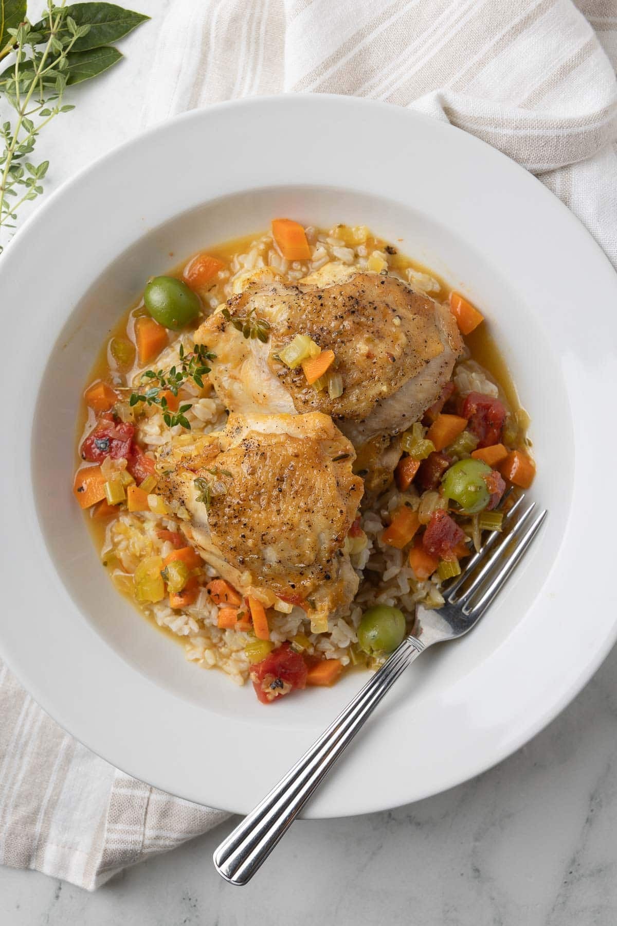 A bowl of golden chicken thighs surrounded by vegetables and sauce, on top of rice.