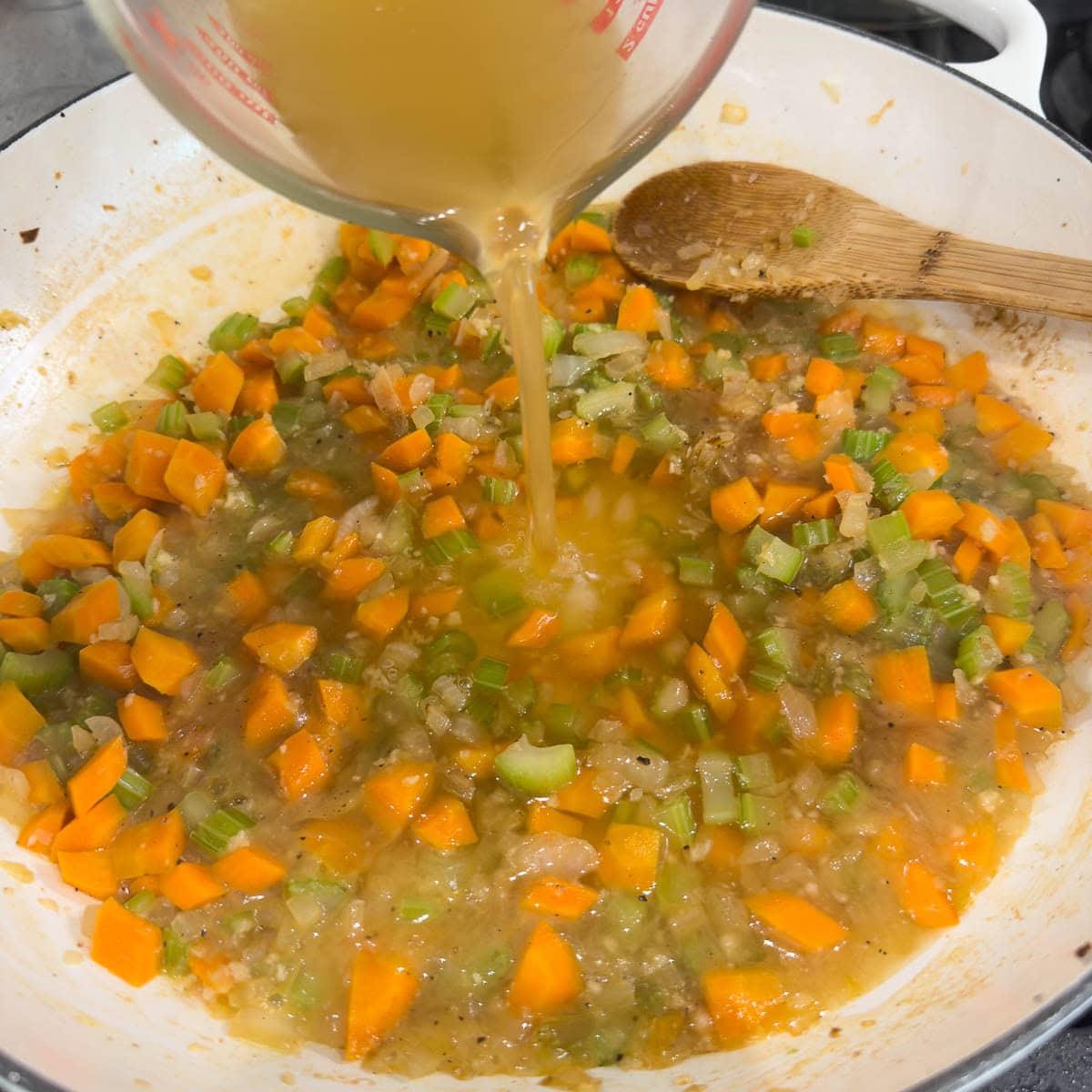 Pouring chicken broth into a pan of vegetables.