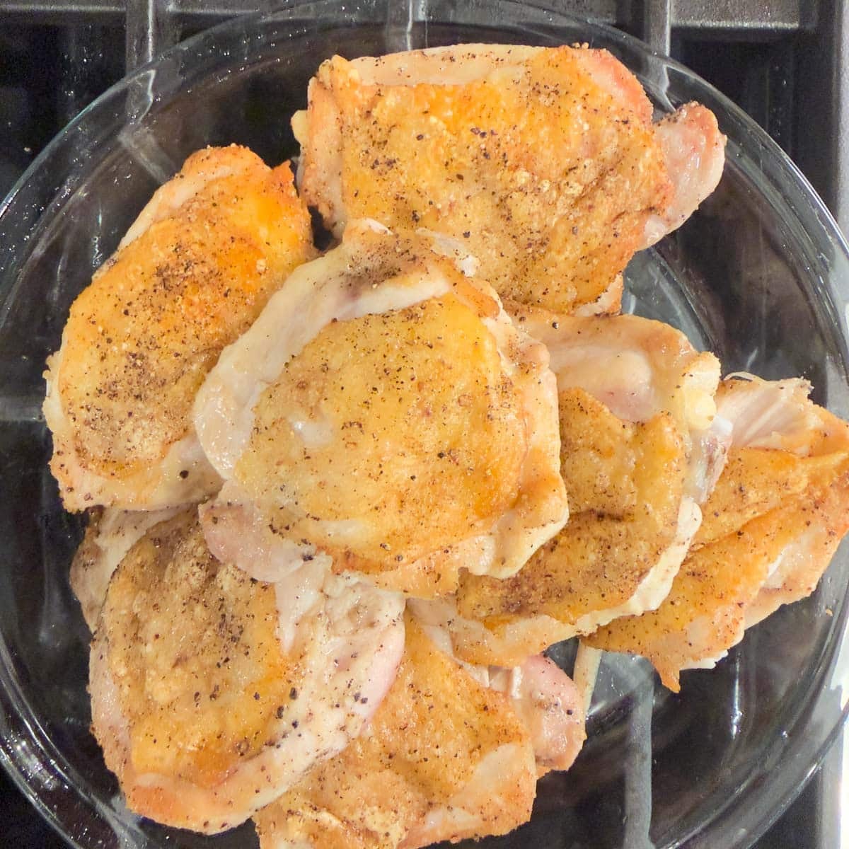 Crisp browned chicken thighs on a plate on stovetop.