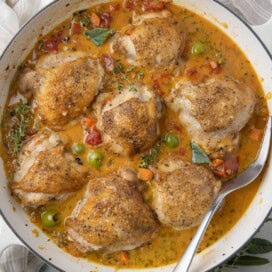 A pan of mediterranean chicken thighs in golden broth with veggies and herbs.