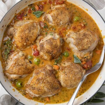 A pan of mediterranean chicken thighs in golden broth with veggies and herbs.