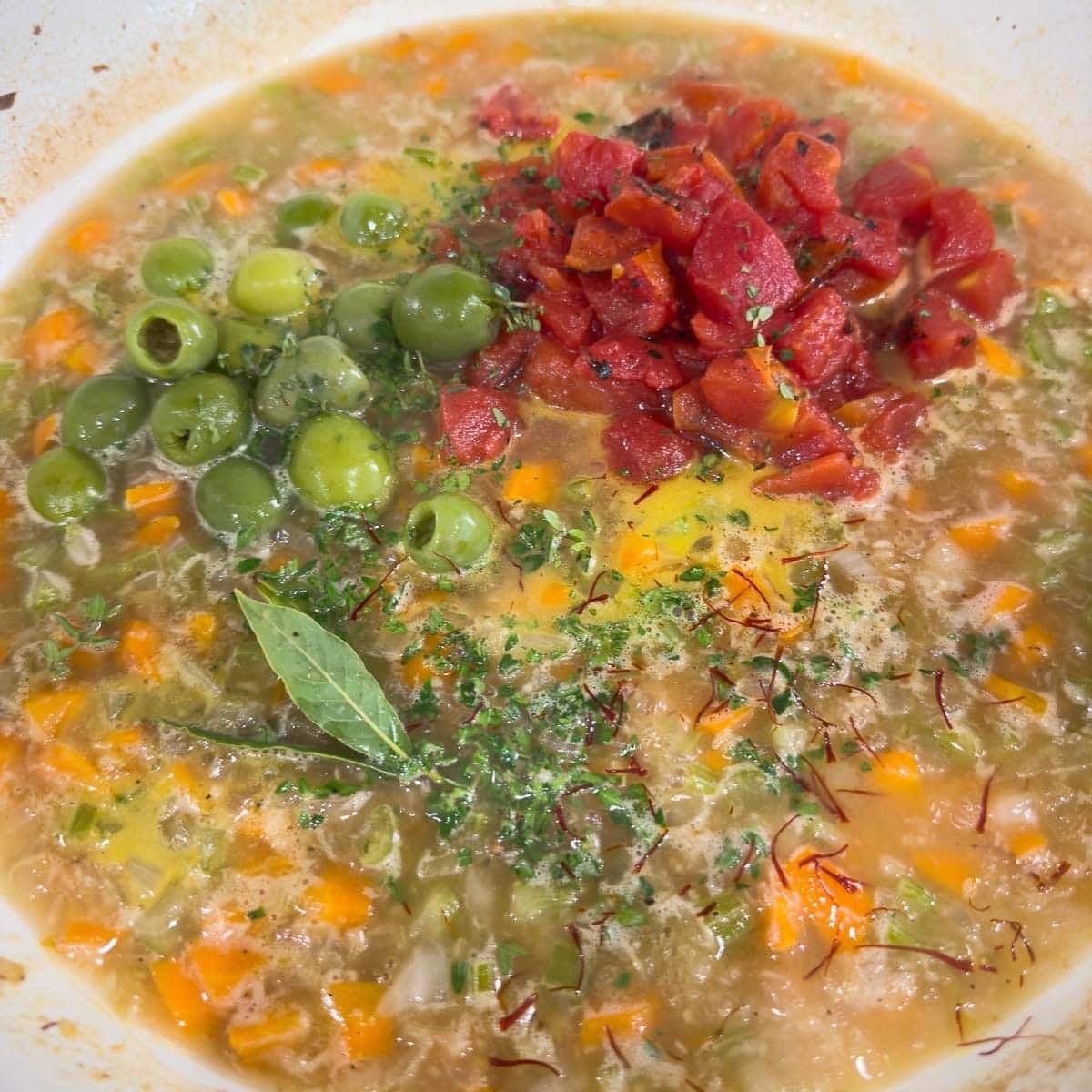 Adding diced tomatoes, herbs, and olives to a pan making mediterranean chicken thighs.