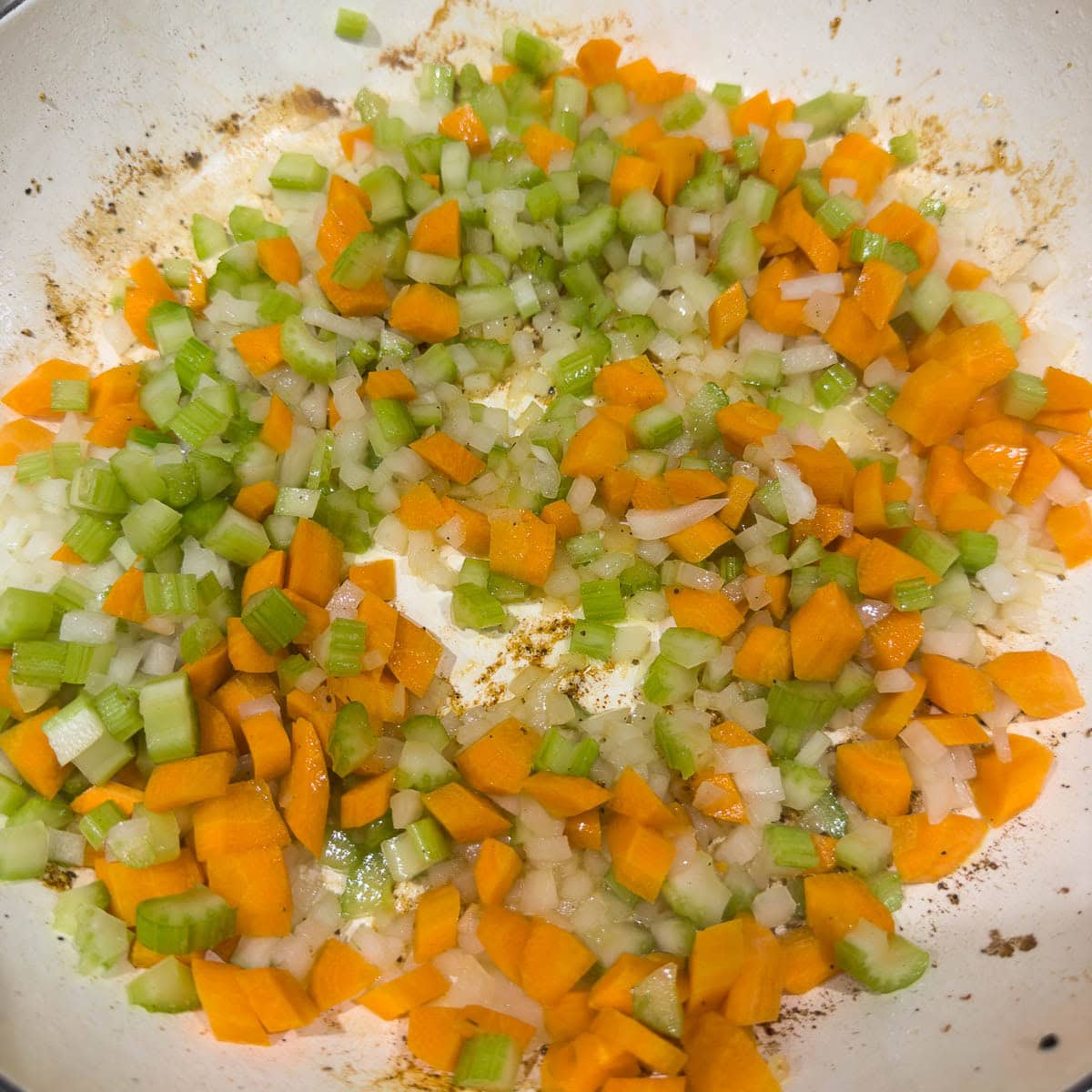 Sauteing onion, carrot, and celery in a large wide pan.