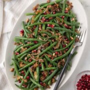 A shallow platter of bright green beans with shallots, pecans, and pomegranate seeds.