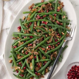 A shallow platter of bright green beans with shallots, pecans, and pomegranate seeds.