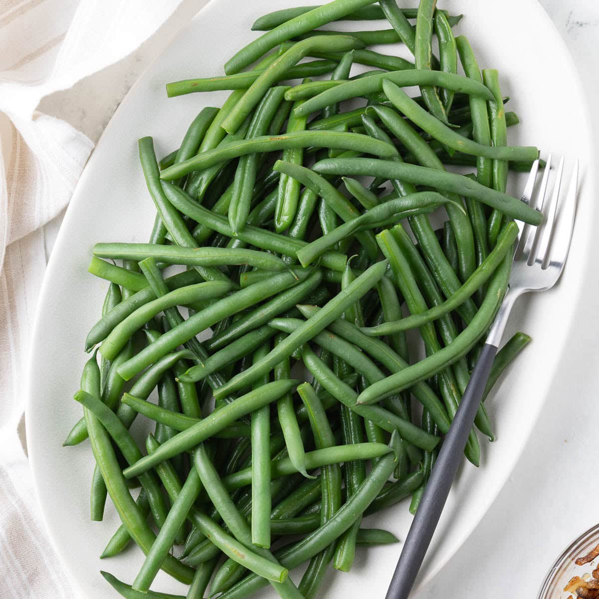 An olva platter of cooked French green beans waiting for the toppings.