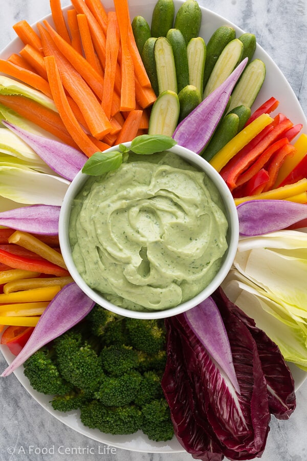 A party platter of colorful vegetables with a bowl of avocado dip in the center.