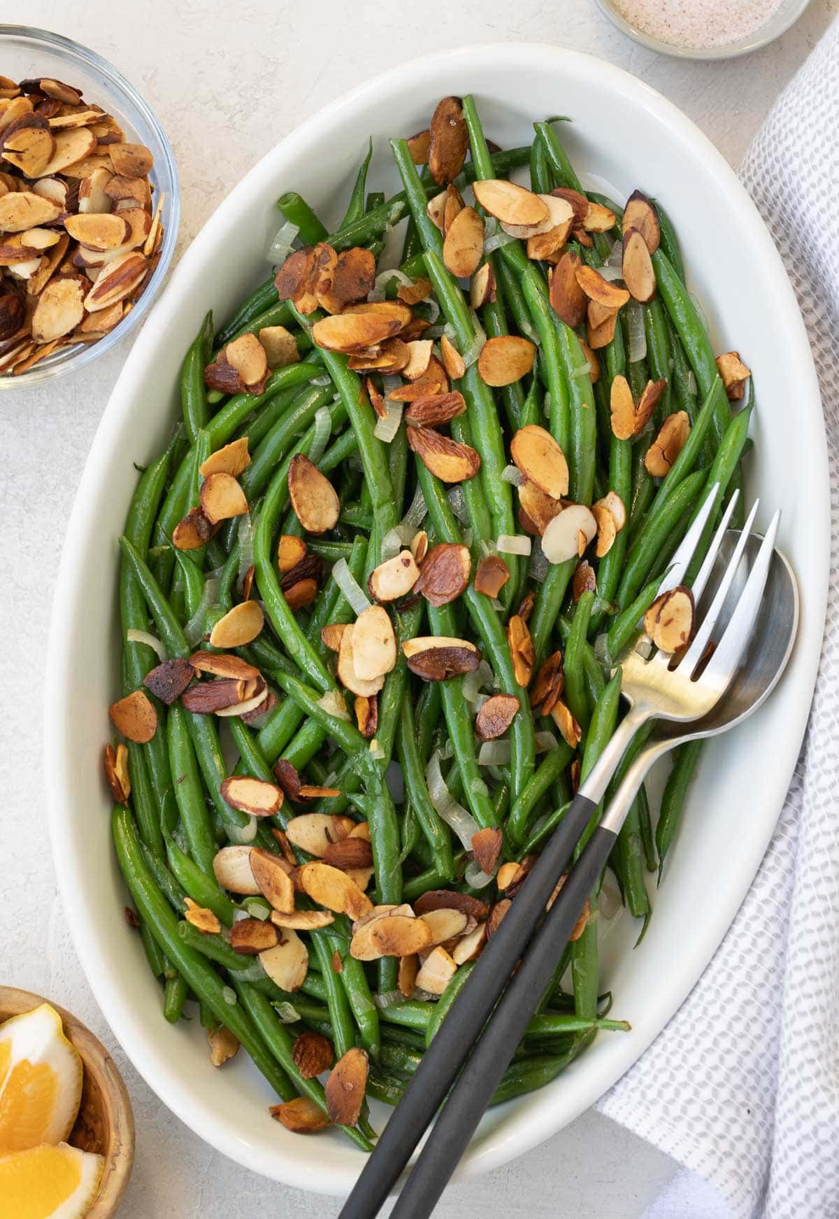 Green beans almondine in a shallow oval bowl scattered with toasted almonds.