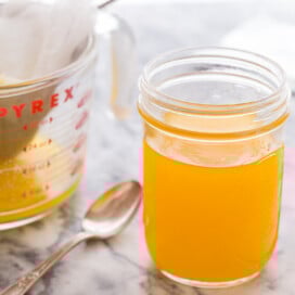 A jar of golden clarified butter on a marble counter with a strainer beside.