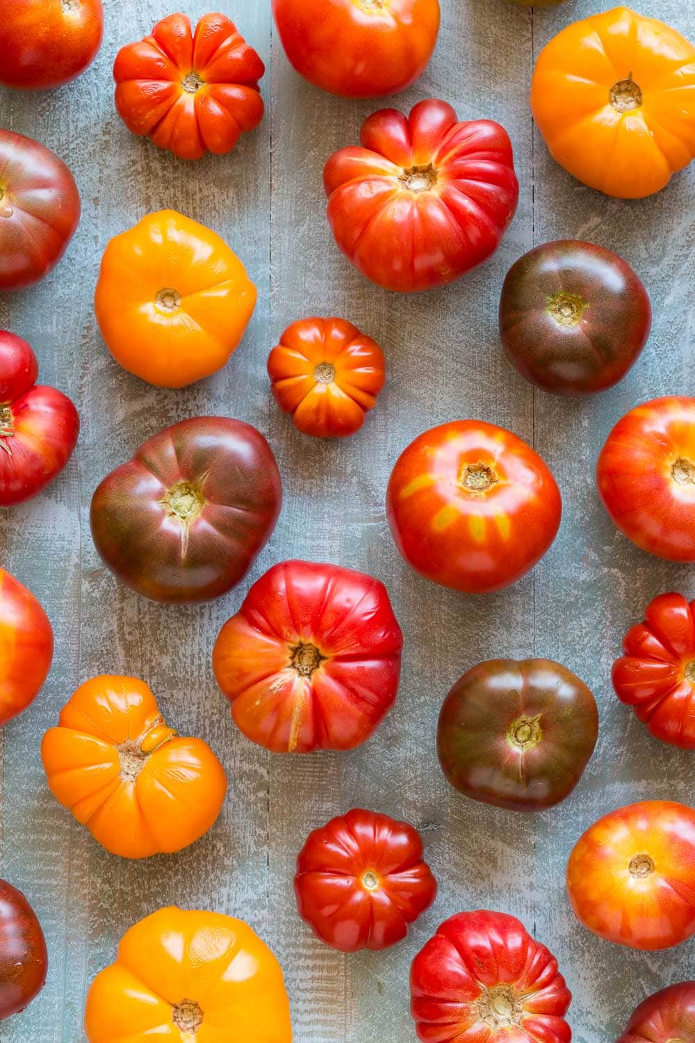 A colorful array of heirloom tomatoes from red to gold to burgundy, on a gray cutting board.