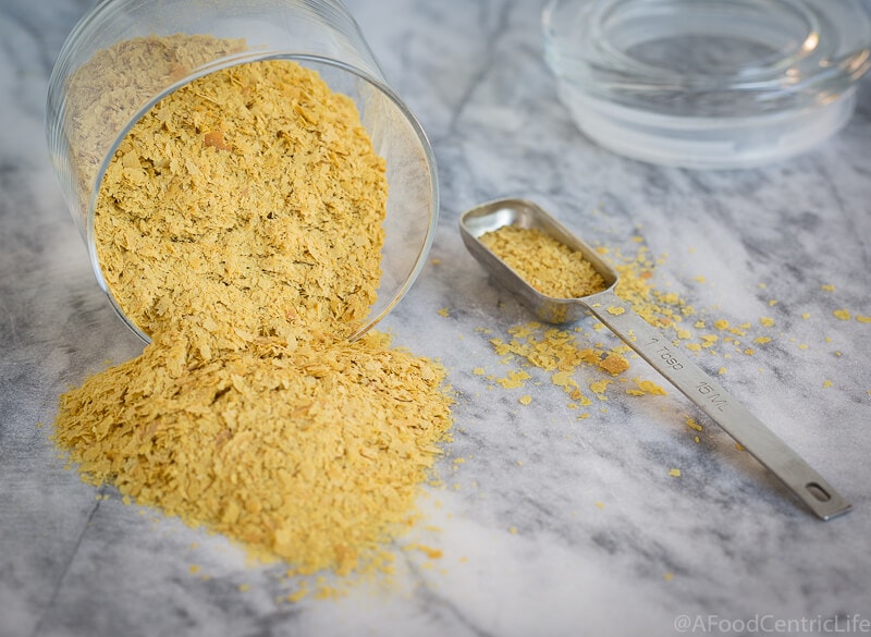 Golden nutritional yeast spilled on a counter with a tablespoon.