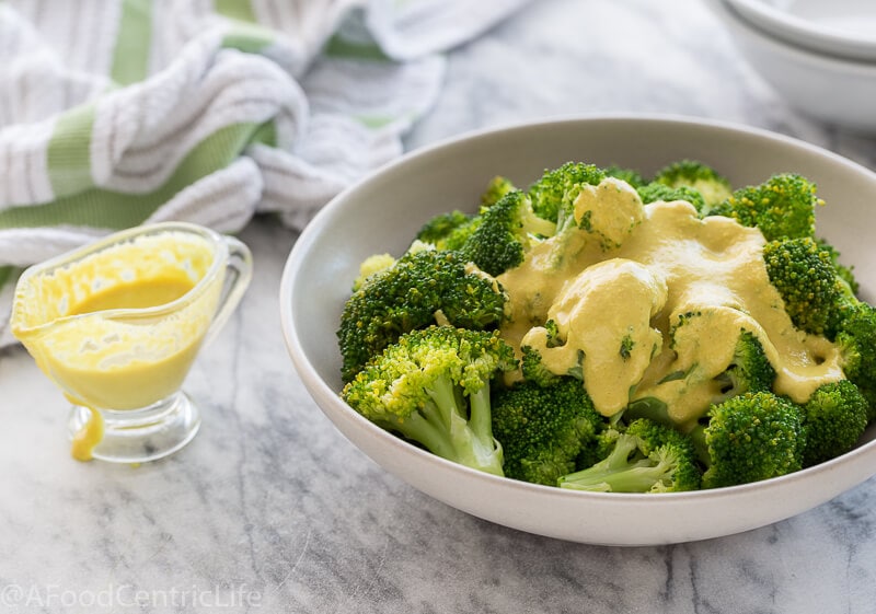 Vegan cheese sauce over bright green steamed broccoli in a bowl. 
