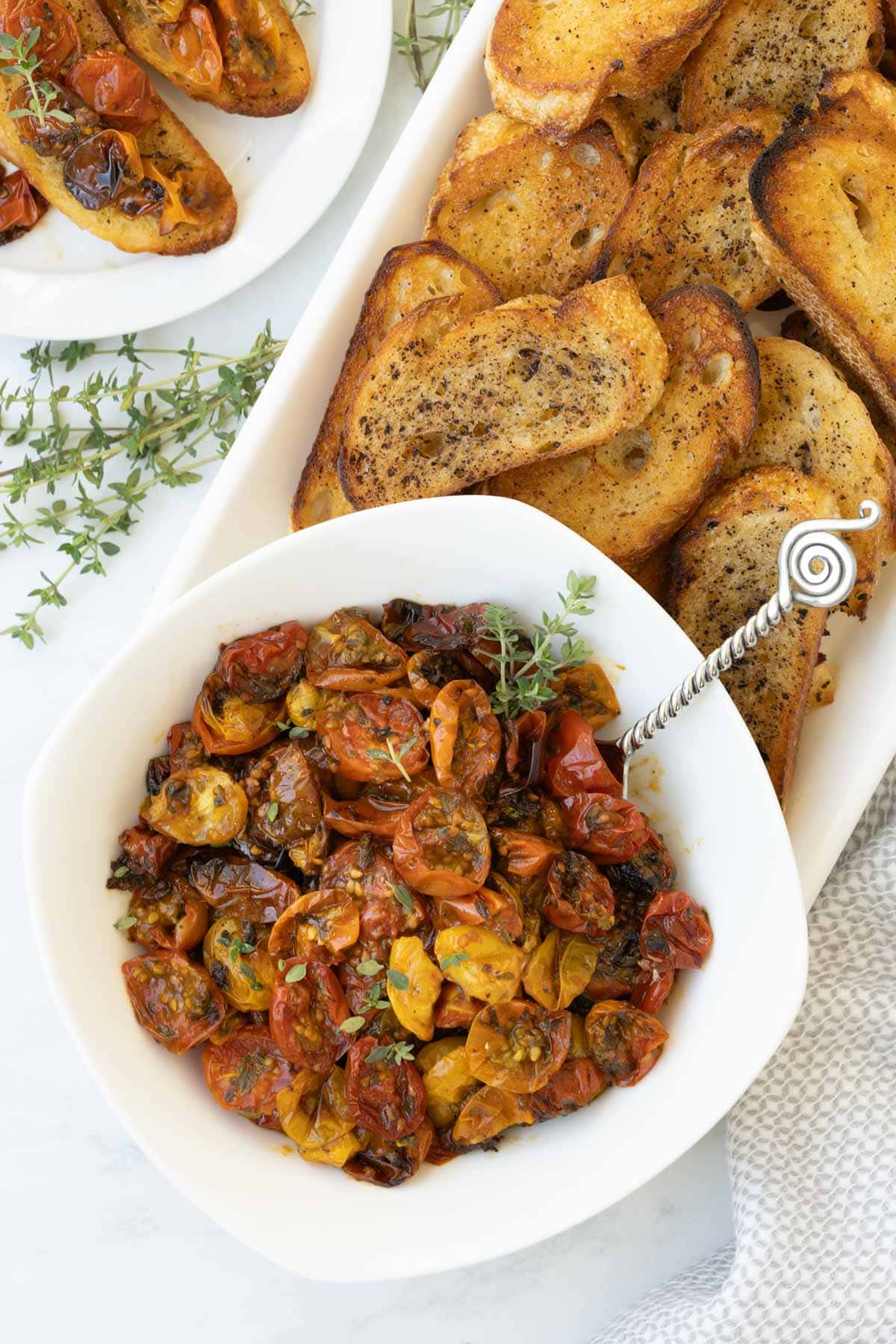 A bowl of colorful oven roasted tomatoes with thyme leaves and golden crostini.