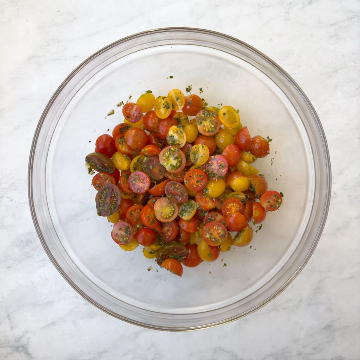 A glass bowl filled with colorful cherry tomatoes tossed with herbs and garlic.