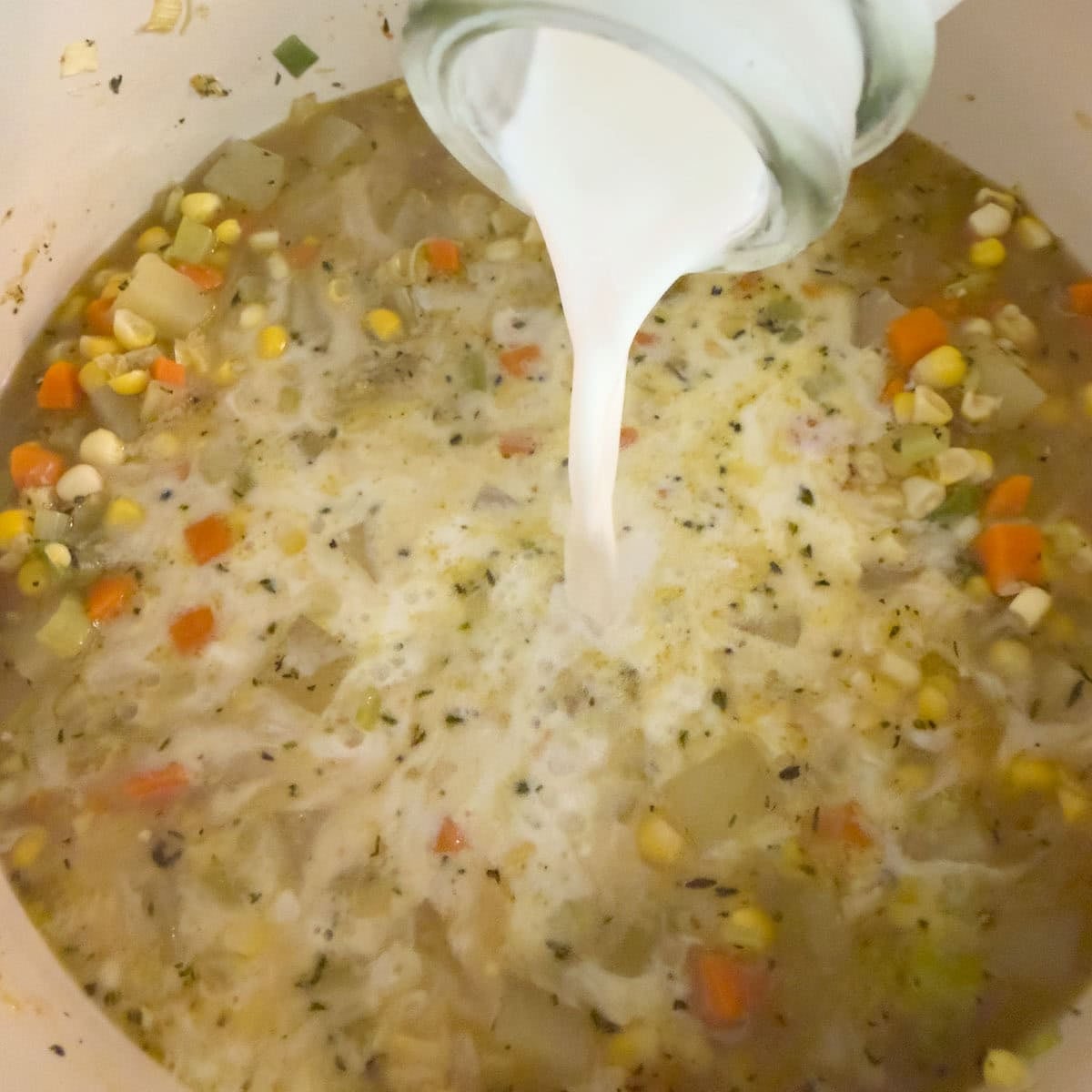 Half and half pouring into a pot of soup from a glass bottle.