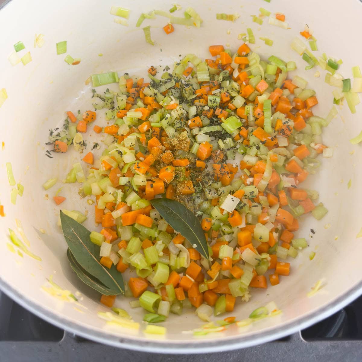 Adding bay leaves and thyme leaves to a pot of cooking vegetables for soup.