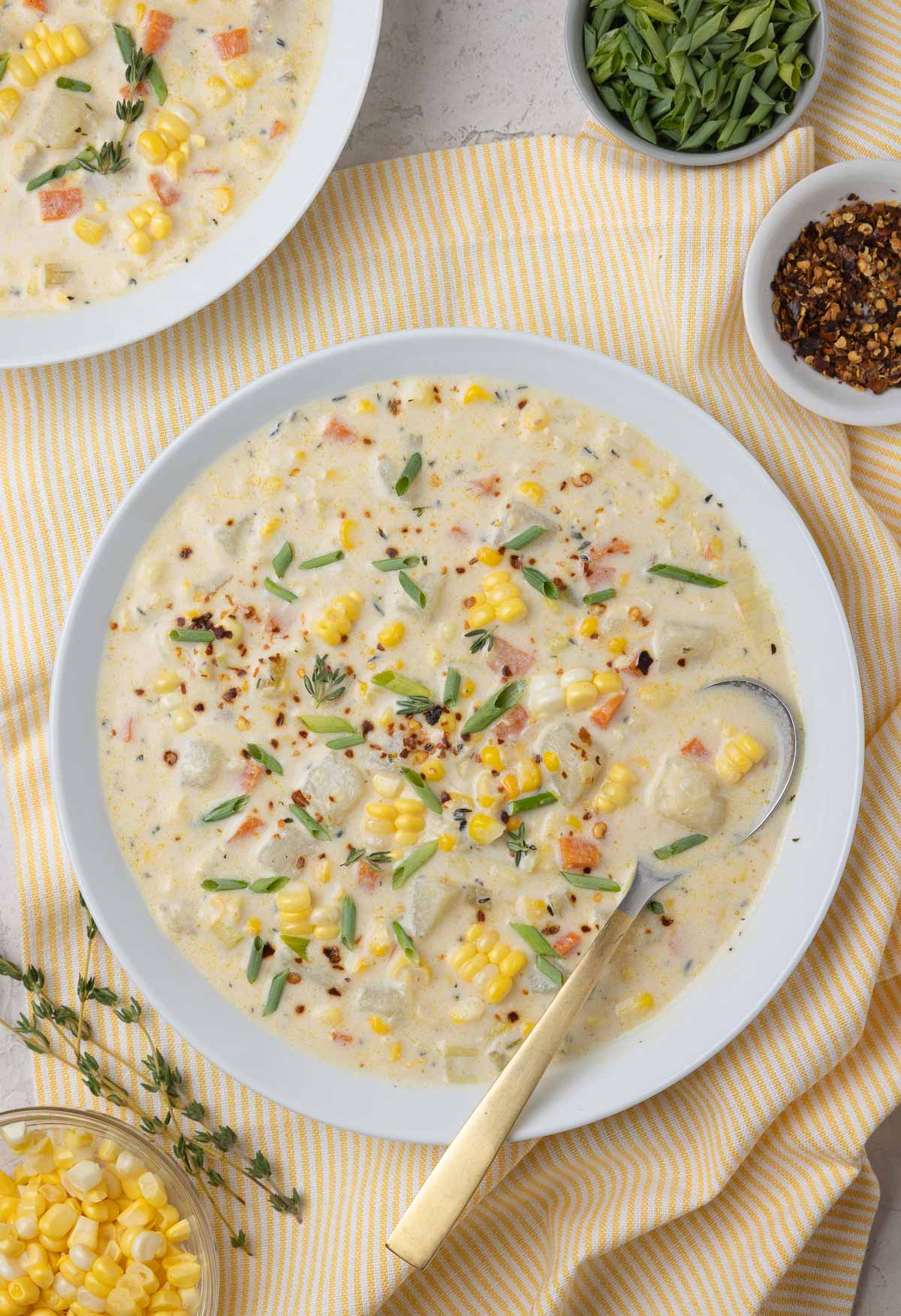Bowls of corn and potato chowder with chives and red pepper, and a gold spoon.
