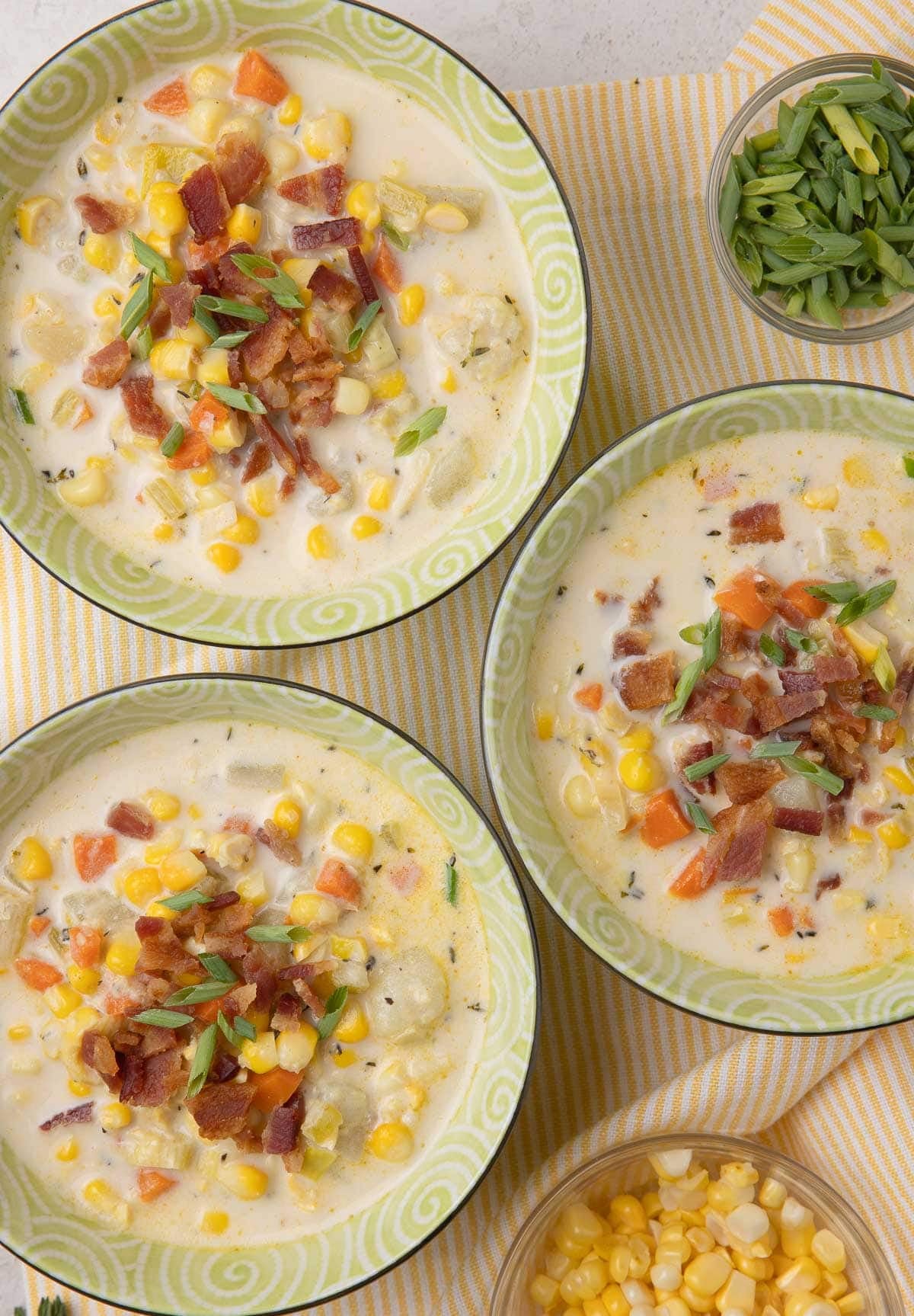 Three small bowls of corn and potato chowder with crumbled bacon and chives.