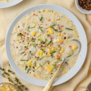 White bowl of creamy potato and corn chowder with a gold spoon.