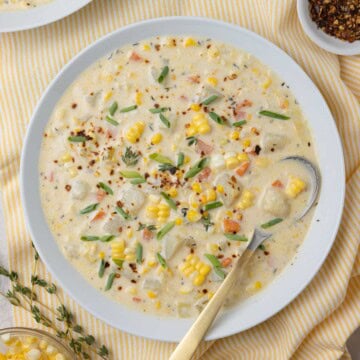 White bowl of creamy potato and corn chowder with a gold spoon.