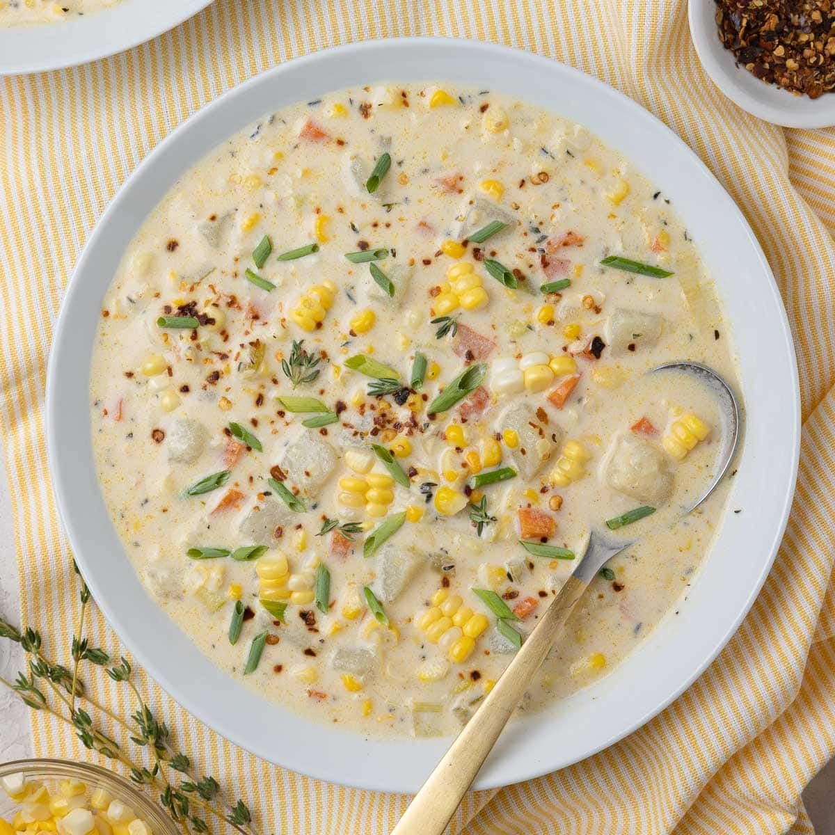 White bowl of creamy potato and corn chowder with a gold spoon.