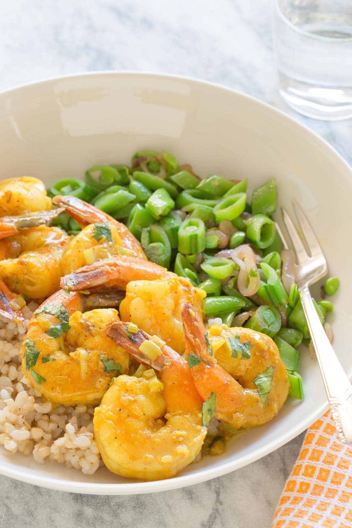 A bowl of coconut curry shrimp served over rice with snap peas.