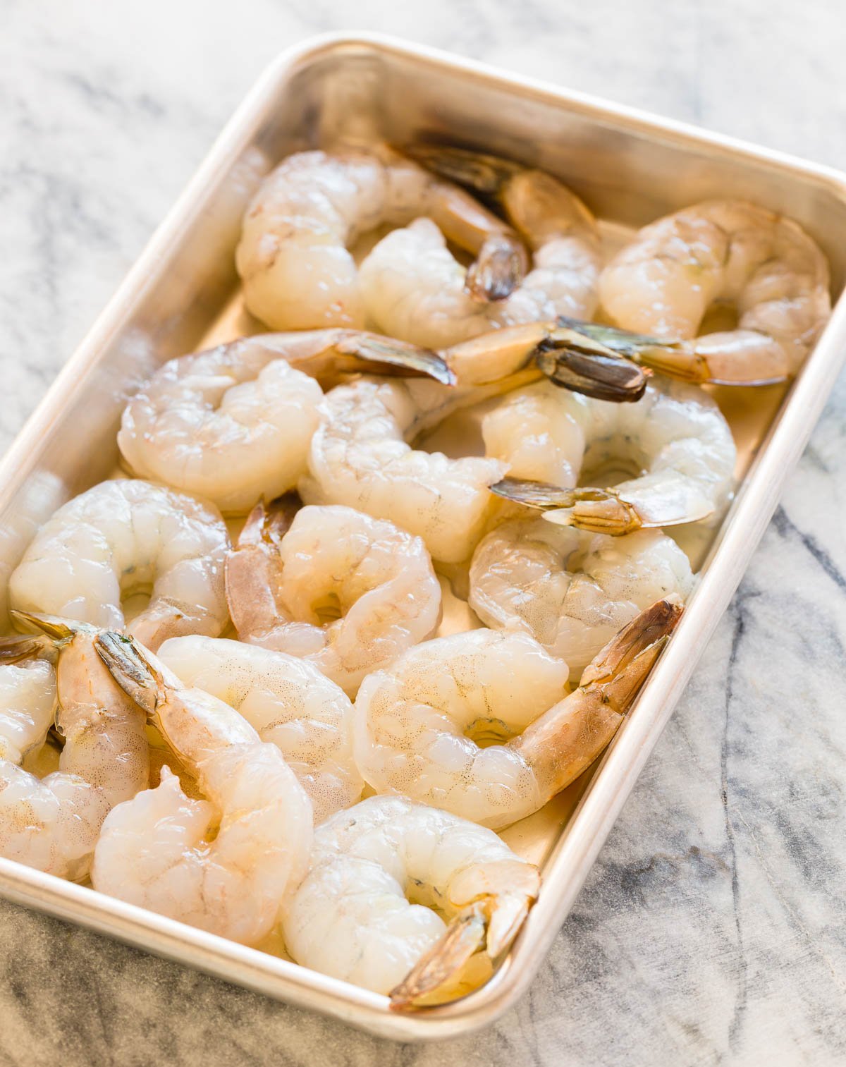 Raw shrimp peeled and cleaned on a rimmed baking sheet.