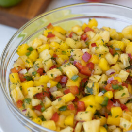 A glass bowl of tropical fruit salsa with pineapple, mango, peppers, and herbs.