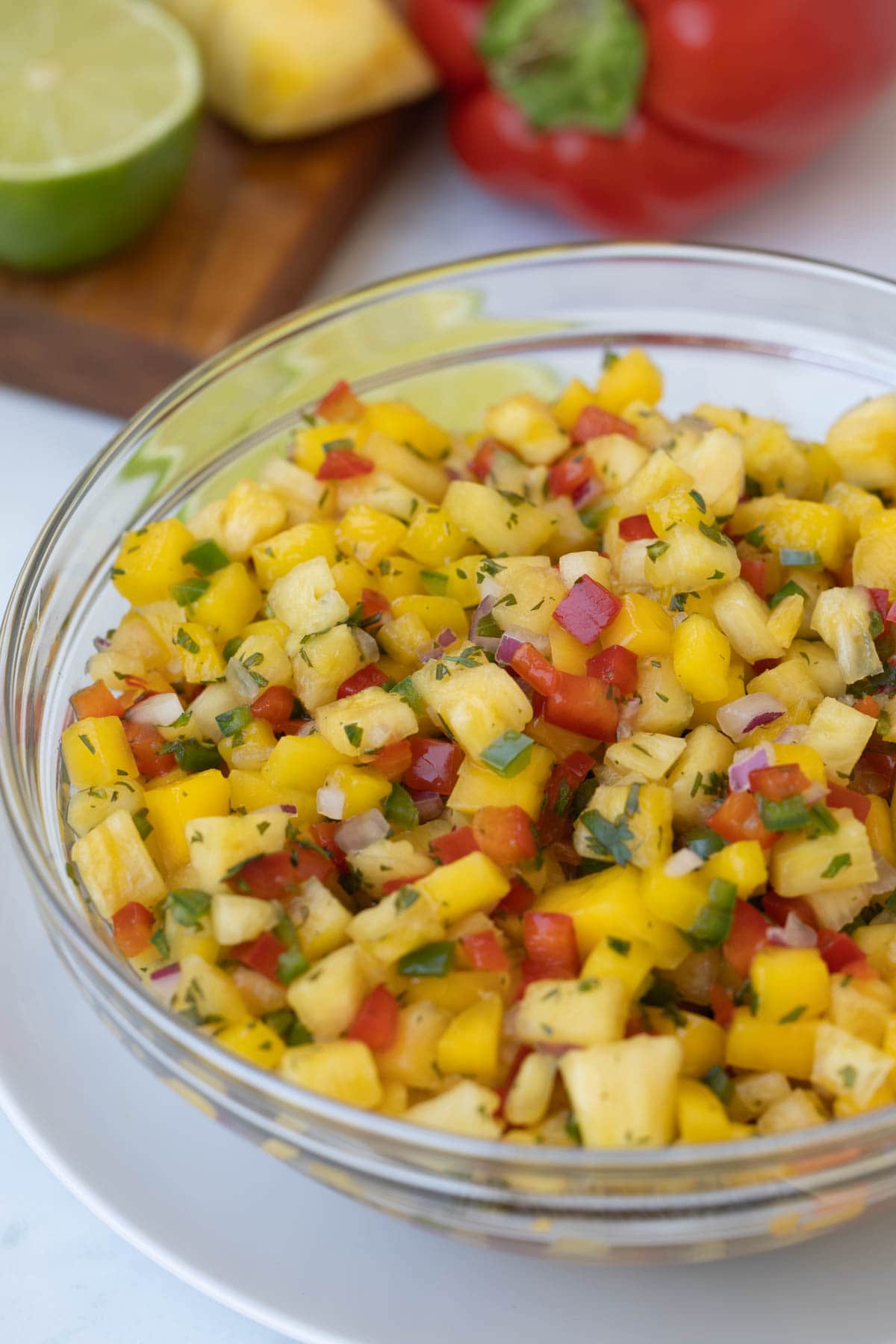 A glass bowl of tropical fruit salsa with pineapple, mango, peppers, and herbs.