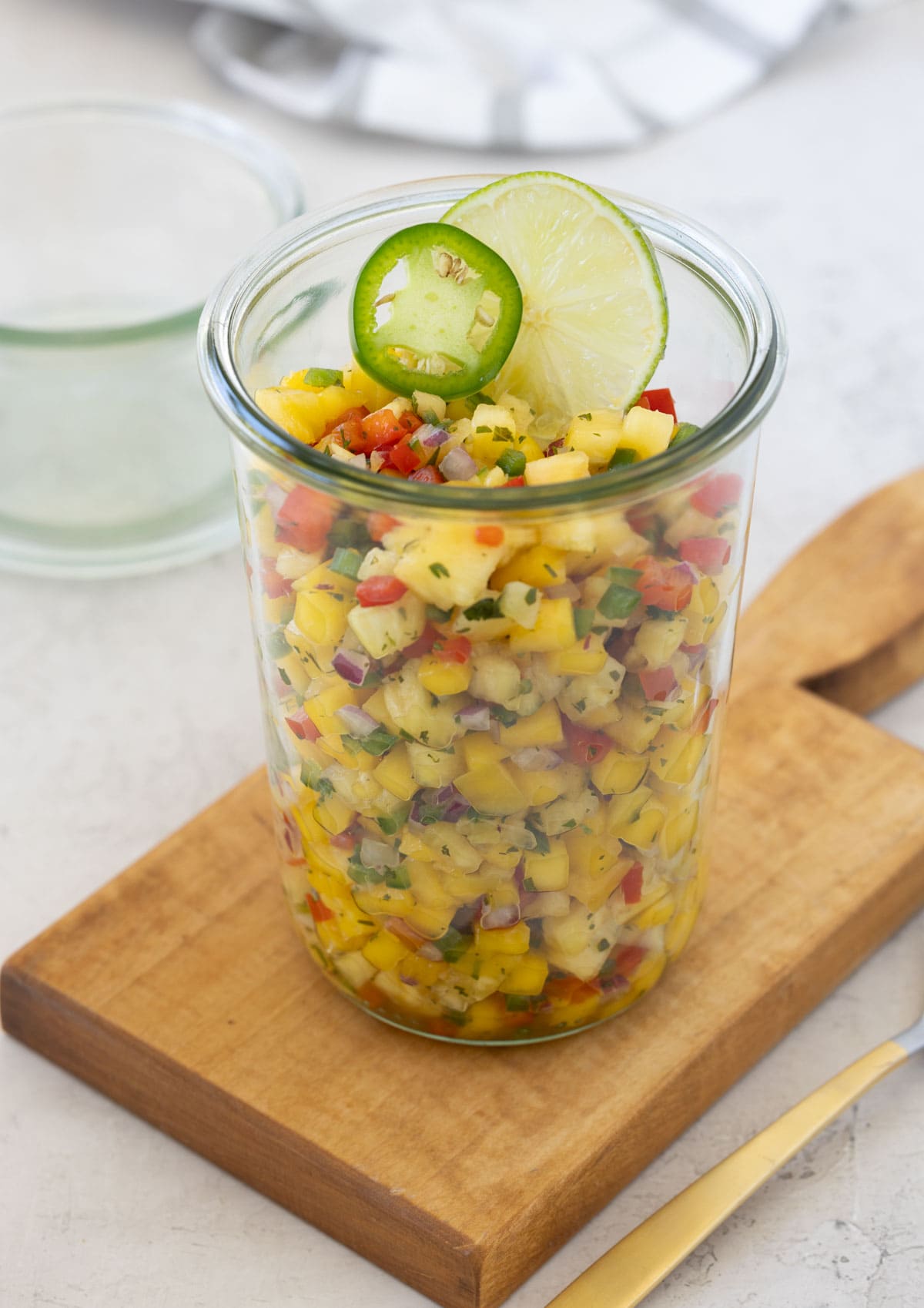 A glass jar of brightly colored pineapple mango salsa.