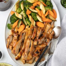 A platter of sliced teriyaki chicken thighs with vegetables.