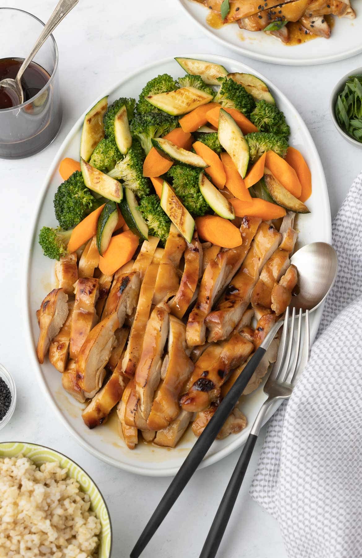A platter of sliced teriyaki chicken thighs with vegetables. 