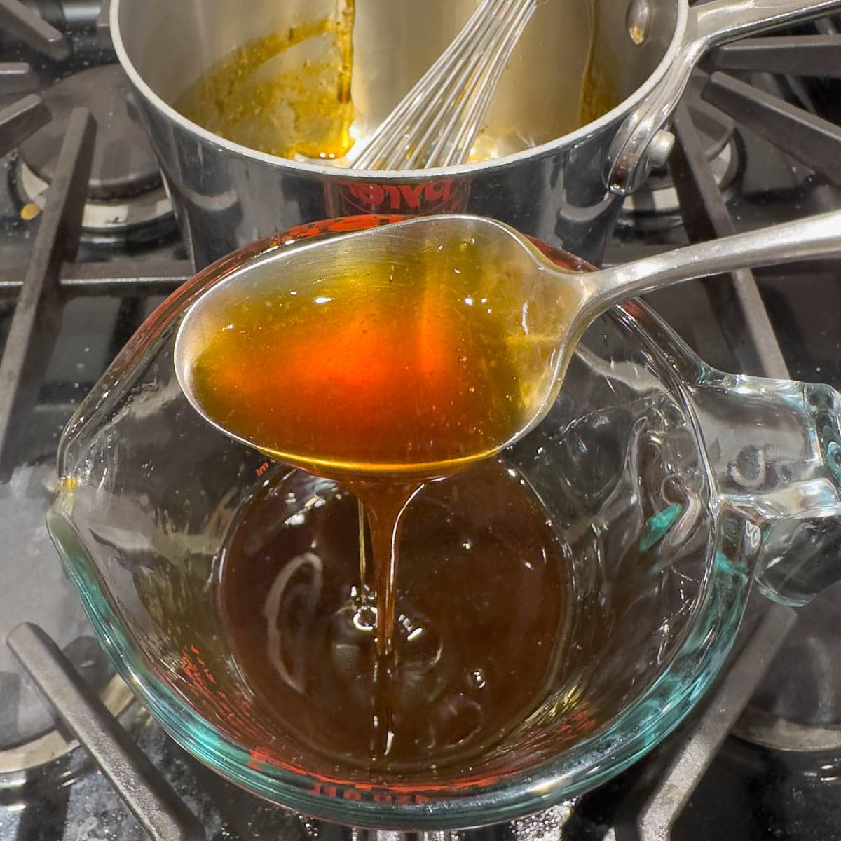 Golden brown finished sauce pouring off a spoon into a container.