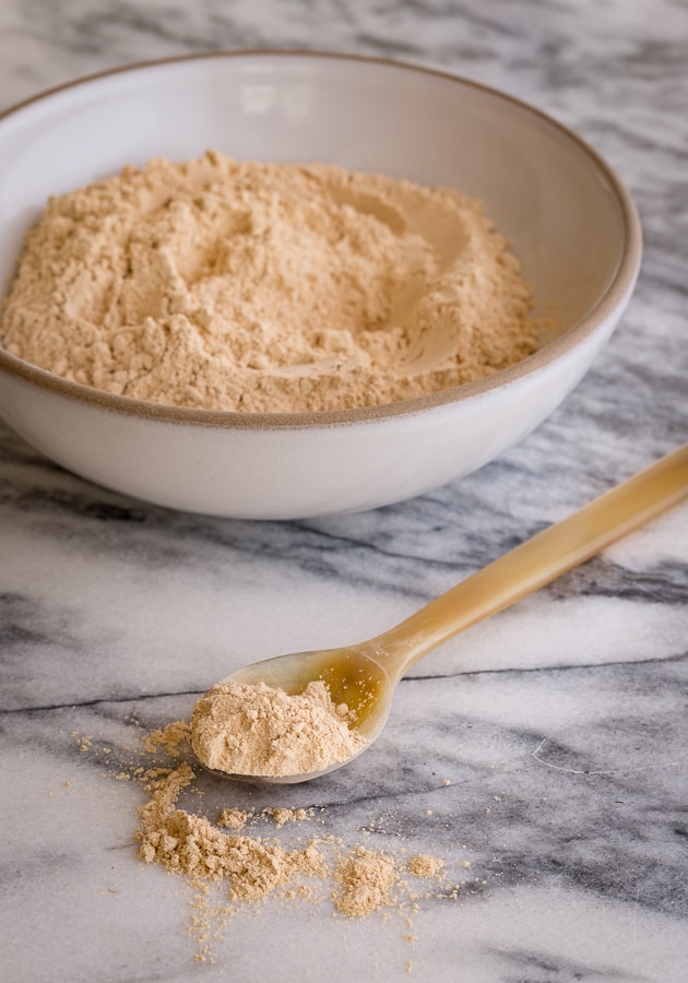 Maca powder in a bowl and spoon on counter.